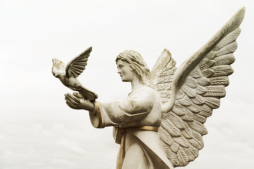 A stone angel releases a dove from her hands (concept: angel of peace)