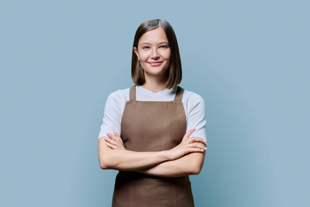 istock Young smiling woman in apron looking at camera on blue studio background 1929651681