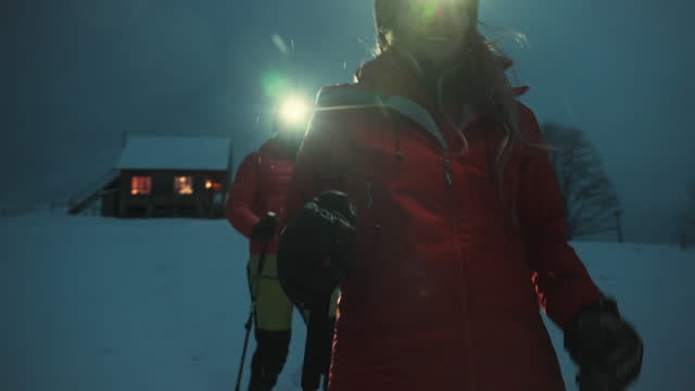 Man and woman hiking on snow at night with headlamps near mountain cabin