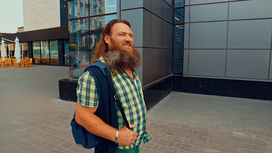 Smiling man with long beard and hair stands next to a gray building