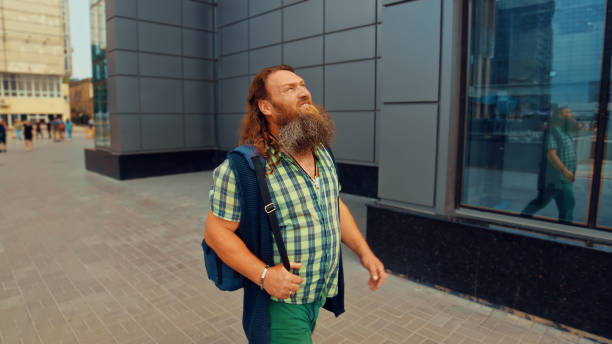 Bearded red-haired man looking up walking along a gray building