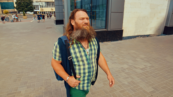 Elderly long-bearded man looks intently into the distance while walking through the city