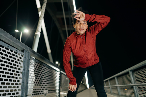A mature woman, having completed her nightly run, takes a well-deserved break on the bridge, her exhaustion mingled with a sense of achievement