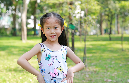 Portrait of happy little Asian child girl with yellow flower on ears in summer garden outdoor.