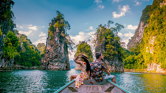 a couple traveling by longtail boat exploring epic limestone cliffs in a huge lake in Khao Sok National Park, Chiew Lan Lake, Thailand Surat Thani, men and woman in front of longtail boat