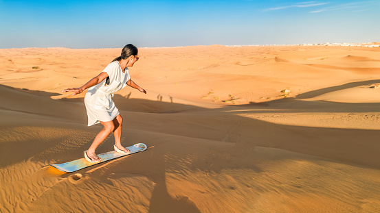 Dubai desert sand dunes, an Asian woman on Dubai desert safari, United Arab Emirates vacation, woman on vacation in Dubai sandboarding at the sand dunes of Dubai