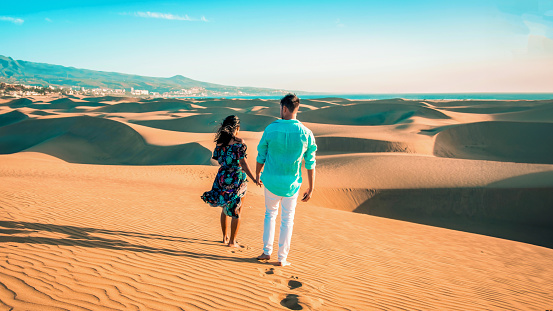 couple walking at the beach of Maspalomas Gran Canaria Spain, men and woman at the sand dunes desert of Maspalomas Spain Europe in the morning sun during sunrise