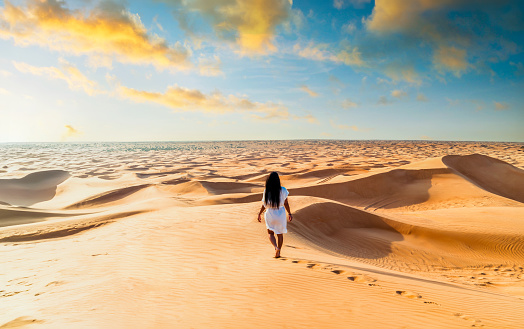 Dubai desert sand dunes, an Asian woman on Dubai desert safari, United Arab Emirates vacation, woman on vacation in Dubai walking at the sand dunes of Dubai