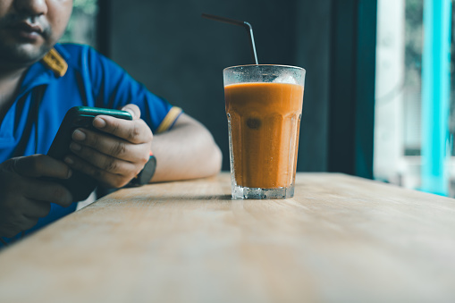 Man drinks cool Thai milk tea while sitting at a table in a cafe enjoying play game or chat in free time.