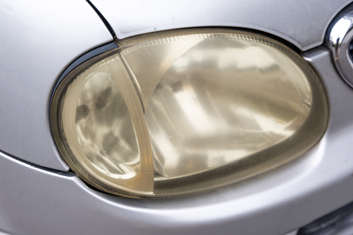 Hazy opaque yellowed front head lamp of car reduces light pass-through and driving visibility on the road