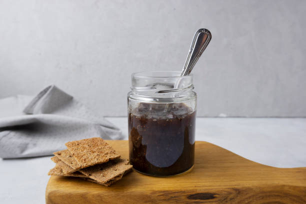 Strawberry jam in a glass jar on a light gray background with sliced bread. Composition with delicious homemade jam. Breakfast and snack concept.