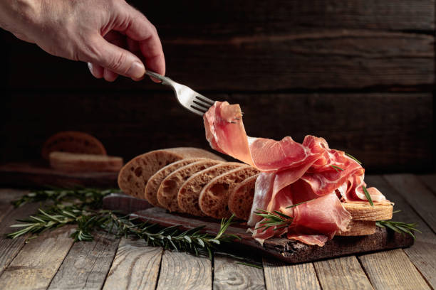 istock Prosciutto with bread and rosemary on an old wooden table. 1929879131