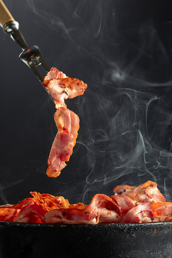 Fried steaming bacon slices on a black background. Copy space.