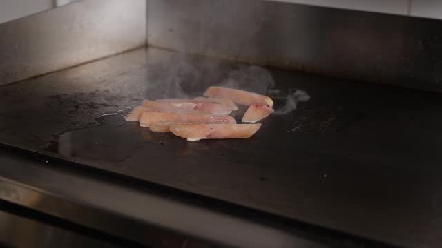 A close-up of the chef puts chicken meat on a stove and covers it with a lid.