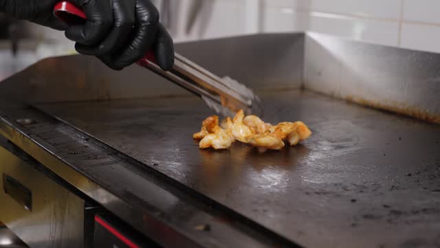 Close-up of the chef frying chicken fillet and turning the meat over with tongs.