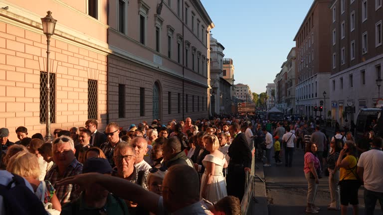 Rome, Italy - 5 September 2023. Wide shot of group tourists and pilgrims queuing to enter Vatican to visit cathedral of St. Peters on sunset.