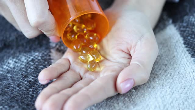 Woman with fish oil pills pours into palm closeup