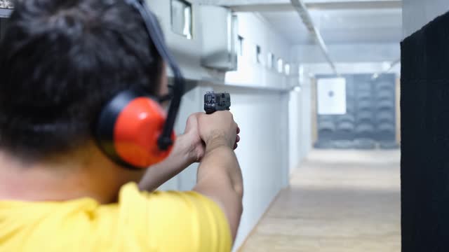 Rear view of man aiming gun at target in shooting range