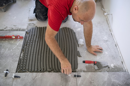 Sweaty tiler spreading adhesive and leveling floor tiles