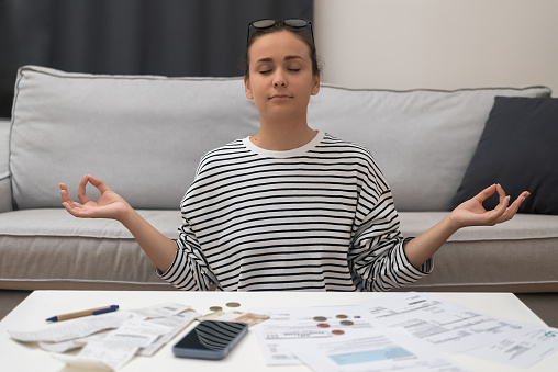 Zen Financial Recovery: A woman meditates in a lotus position, finding inner calm after financial stress from calculating utility bills and taxes.