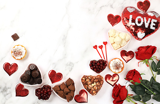 Round baked multicolored macarons lie in a red heart shaped box on wooden background