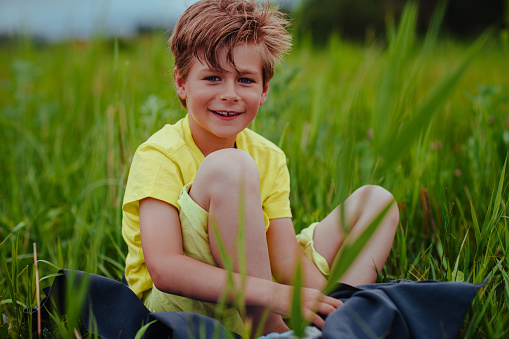 Happy smiling boy sits in the green meadow on towel