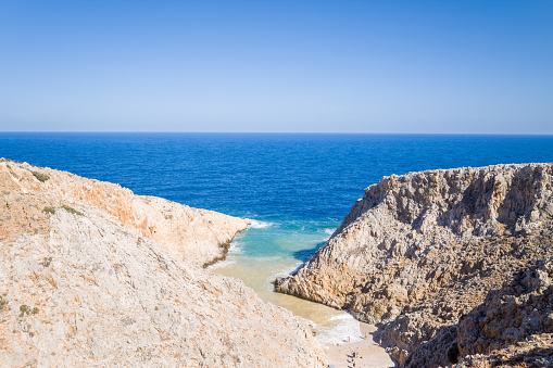 This landscape photo was taken, in Europe, in Greece, in Crete, on the peninsula of Akrotíri, towards Chania, At the edge of the Mediterranean Sea, in summer. We see Seitan Limania Beach in the middle of the rocky cliffs, under the sun.