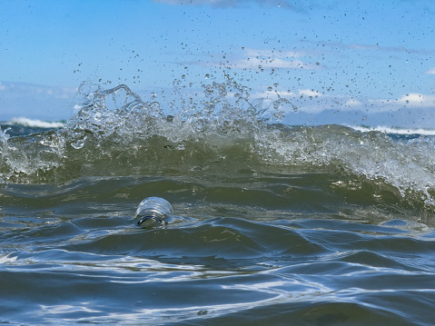 Plastic Bottle Waste floating in the Ocean between waves splashing