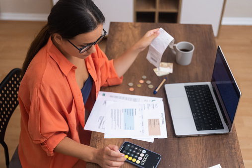 Accountant lady counts bills calculating household finances or taxes on mobile phone calculator at home office woman deals with disposal of family finances