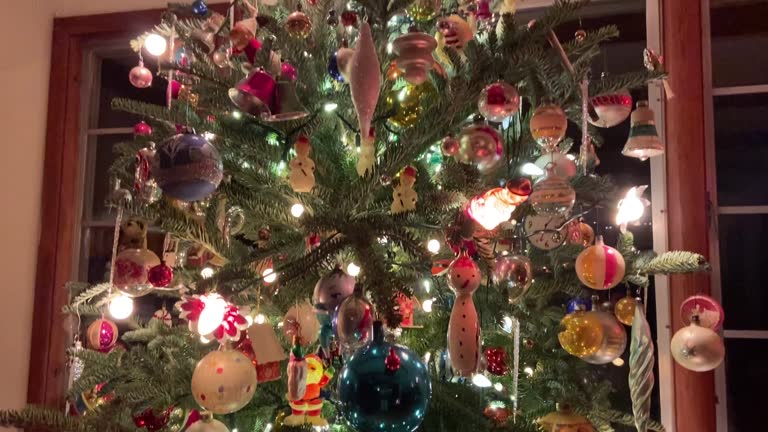 Tilting shot of a Christmas tree decorated with ornaments and string lights at night