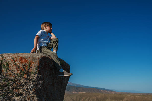 Boy sits on a huge stone in the mountains and looking away