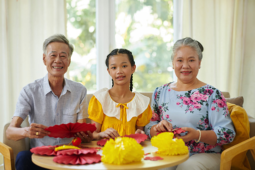 Teenage girl and her grandparents making paper decorations for Lunar New Year