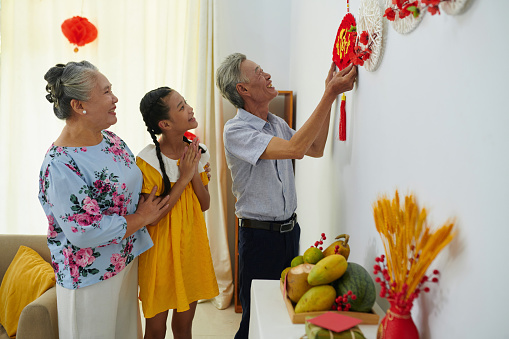 Grandparents and granddaughter decorating apartment walls with traditional ornaments
