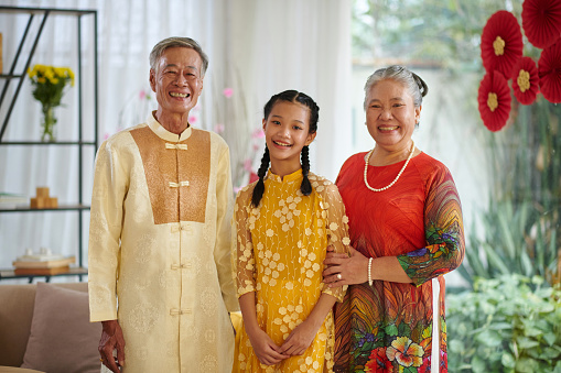 Portrait of happy grandparents and their teenage granddaughter wearing traditional Tet costumes