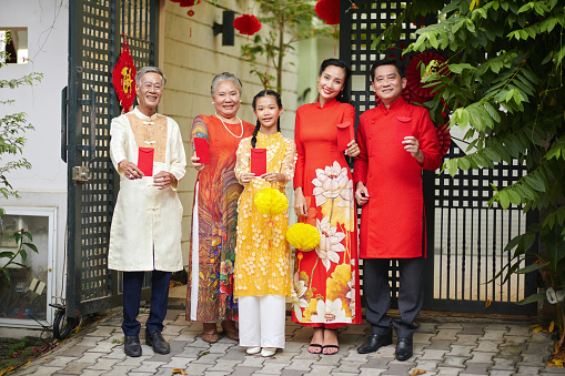 Happy family showing red envelopes with lucky money when standing in front of house gates