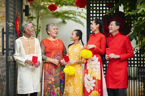 Happy Vietnamese family with red envelopes standing in front of house gates