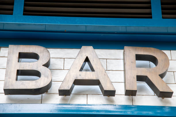 The word Bar on a faÃ§ade in bronze-colored letters. The wall is tiled in white. The letters will have a slight shadow