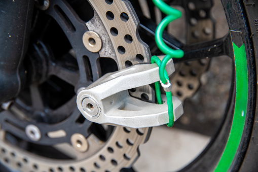 A brake disc lock on a cast aluminum brake disc. The owner's green reminder tape is attached to the lock to prevent accidental driving off.