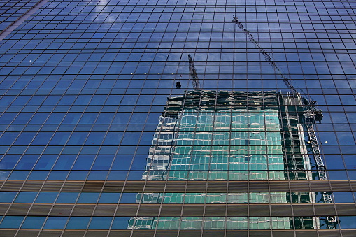 Building under construction with crane on the top, reflected on a modern glass skyscraper, Singapore
