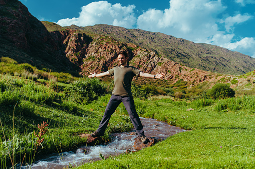 Man hiker standing and balancing on both sides of a mountain stream