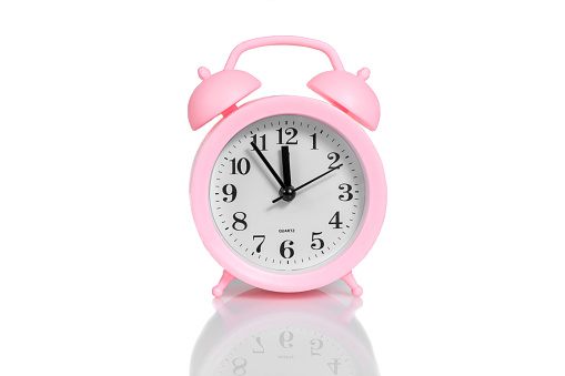 pink alarm clock set twelve o'clock isolated over white background close-up