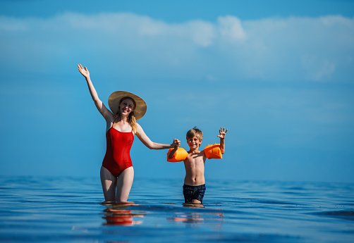 Happy young woman and her son waving hands in the sea