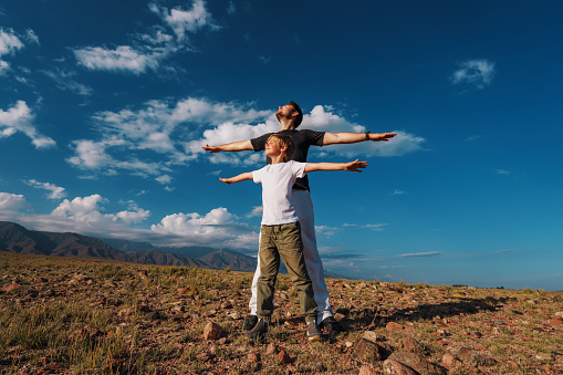 Happy father and son standing on mountains background, enjoying freedom