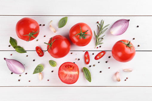 Flat lay composition with whole and cut tomatoes on white wooden table