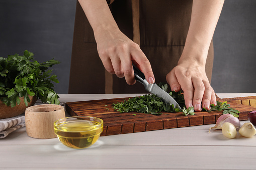 Woman cutting fresh parsley at white wooden table, closeup