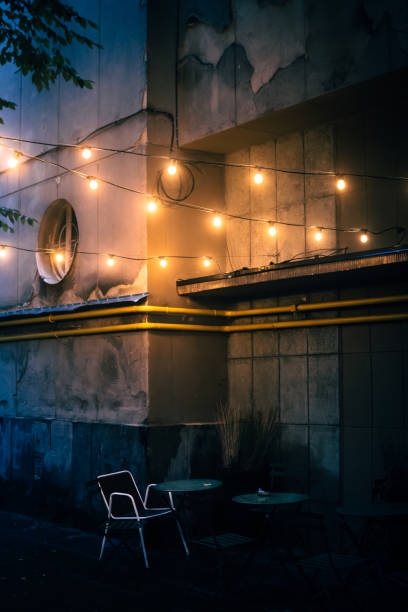 An empty white chair standing by a table under bright warm lightbulbs. Cinematic tones.