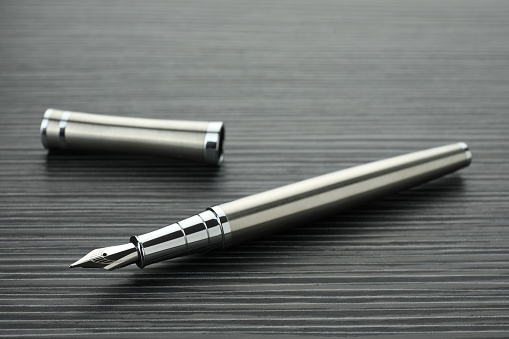 Stylish silver fountain pen on black wooden table, closeup