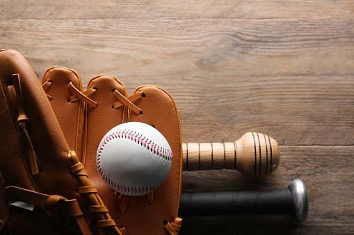 Baseball glove, bats and ball on wooden table, flat lay. Space for text