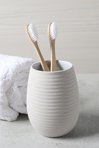 Bamboo toothbrushes in holder and soft towel on light grey table