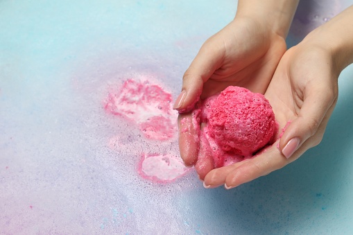 Woman holding bath bomb over water with foam, closeup. Space for text